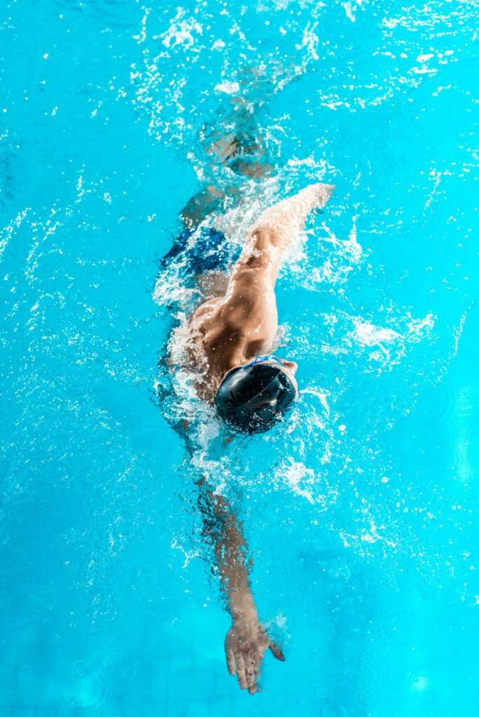 athletic swimmer in cap and goggles swimming in pool