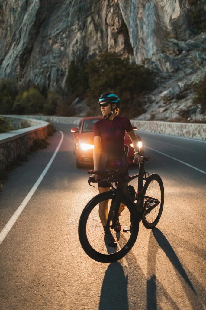 Portrait of cyclist woman with road triathlon bike in headlights of car in twilight
